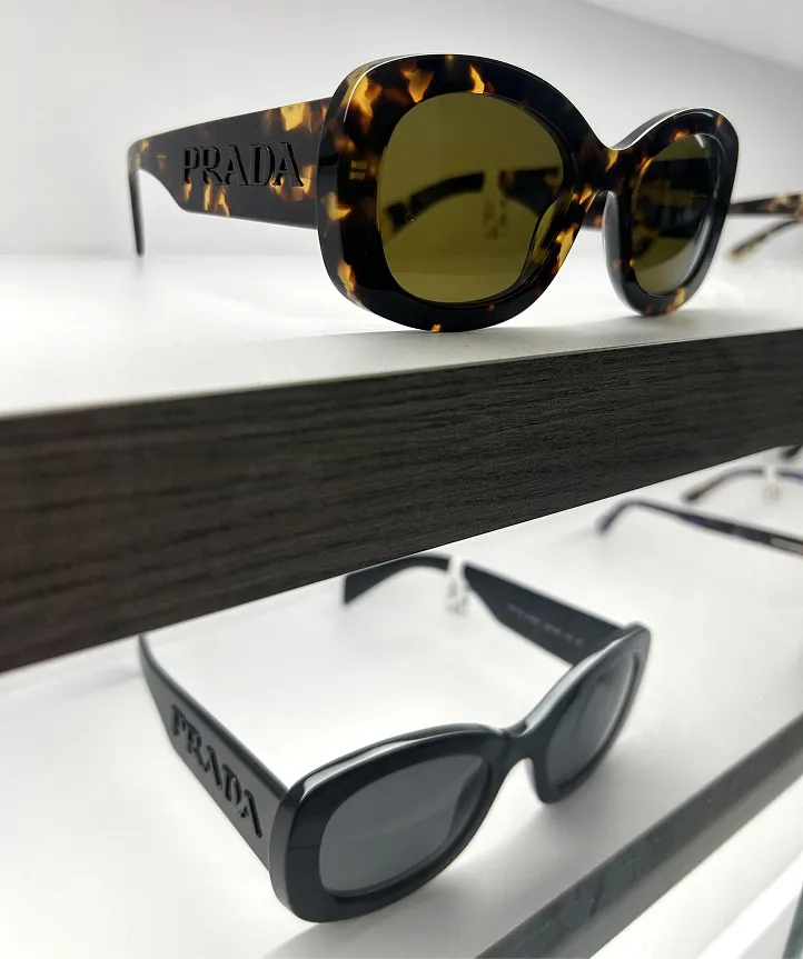 Two Prada sunglasses with tortoiseshell and black frames on shelves