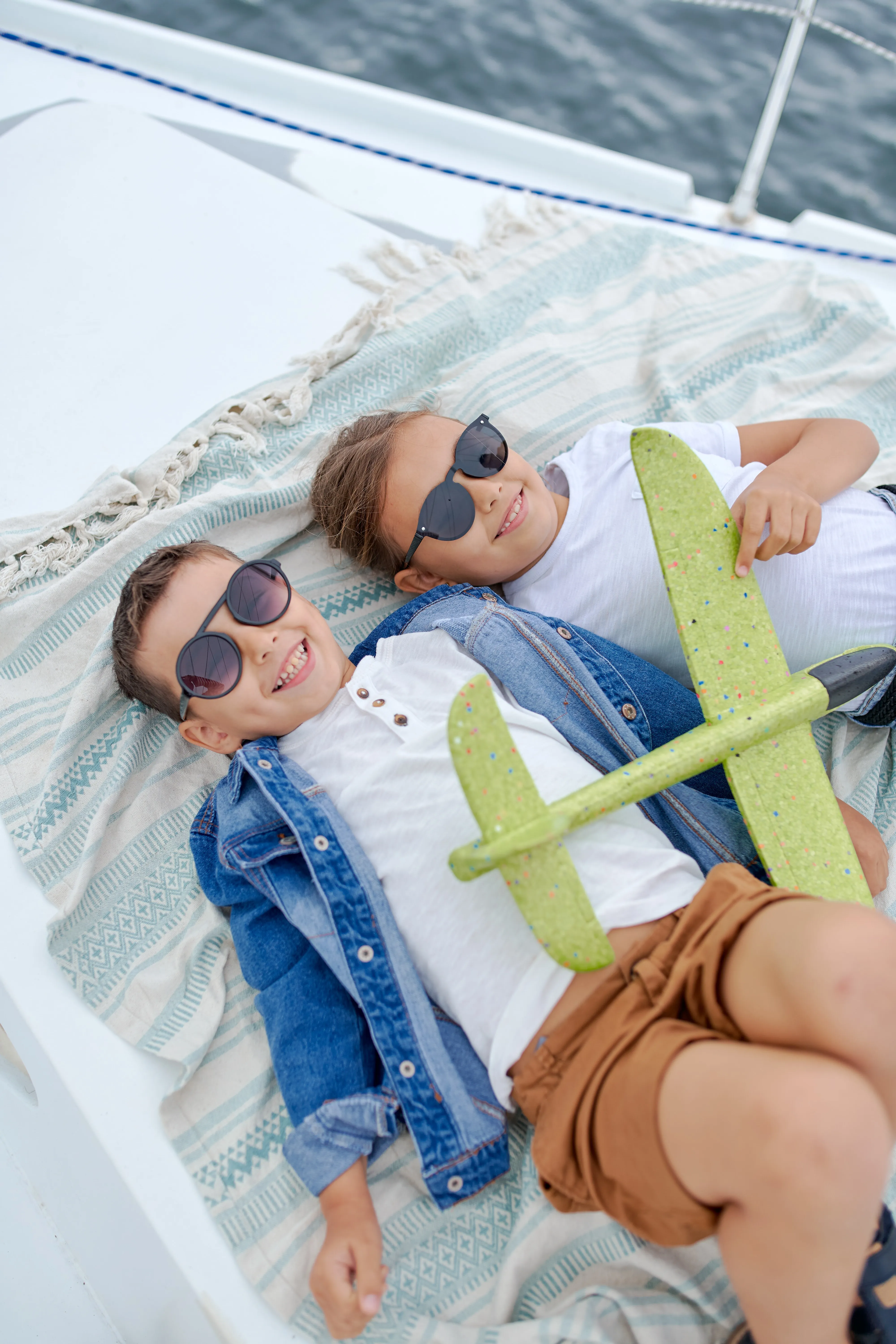 Two children in sunglasses relaxing on boat with green toy airplane