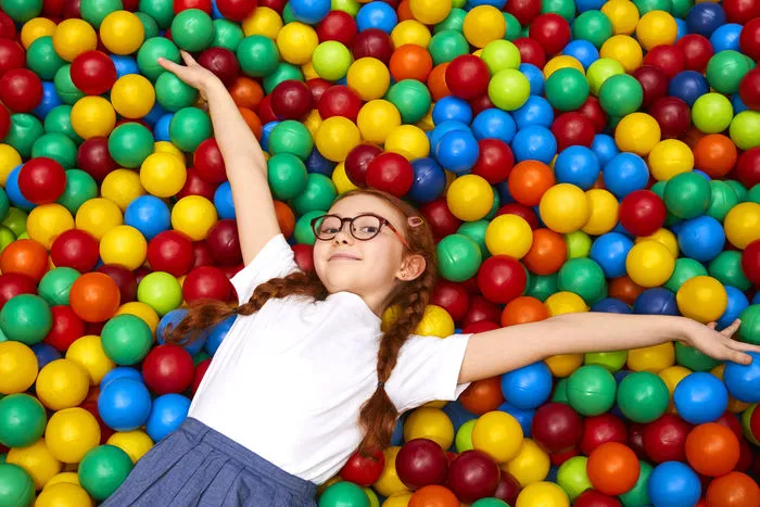 Child lying happily in colorful ball pit with arms spread wide