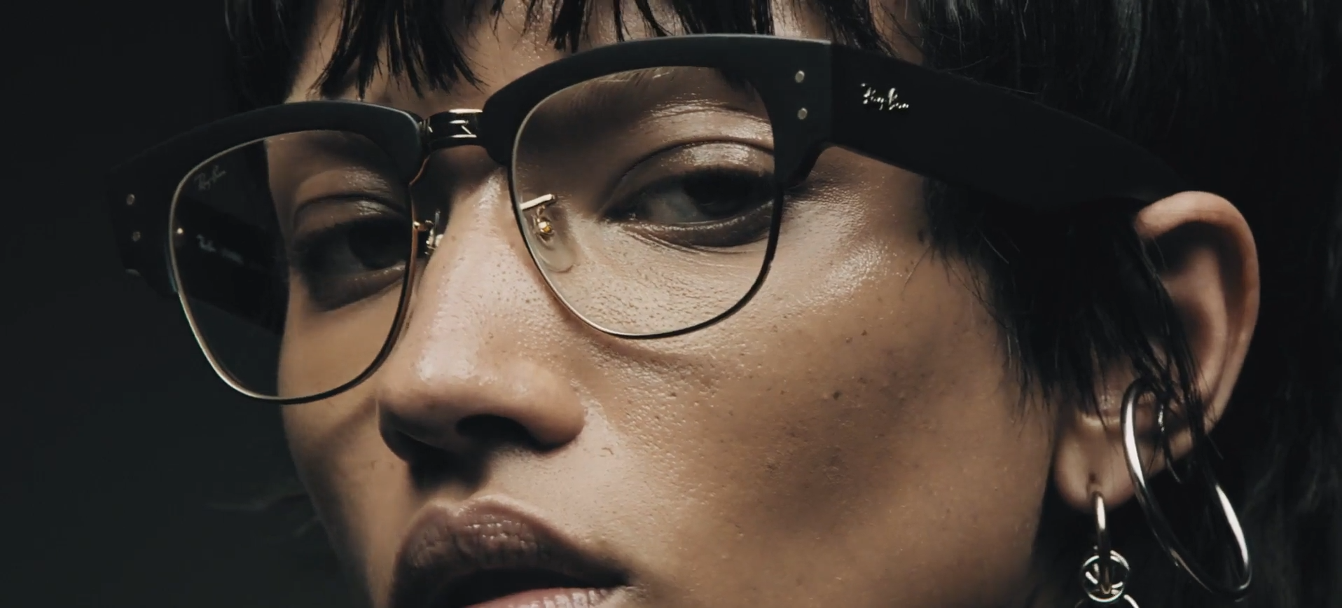 Close-up of person wearing large black-rimmed glasses with moody lighting