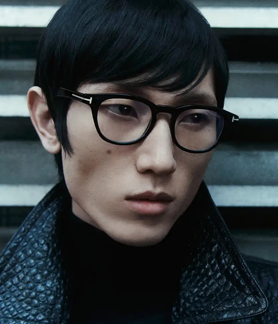 Person with glasses and black hair in textured coat against striped background