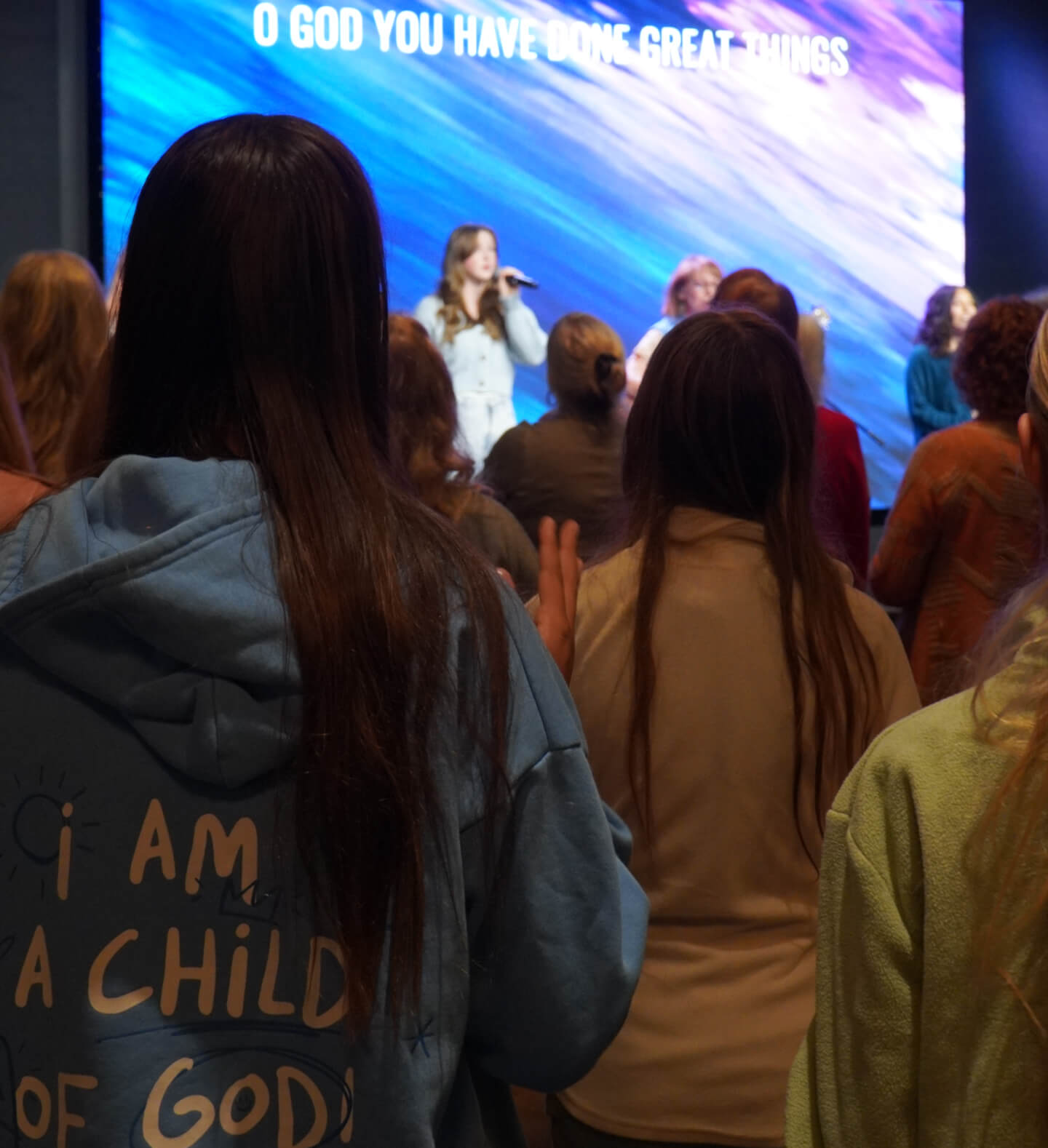 A bold screen background showing colors of cerulean, lavender, and fuchsia while women of various ages are worshipping at Harvest Church’s Worship Nights event