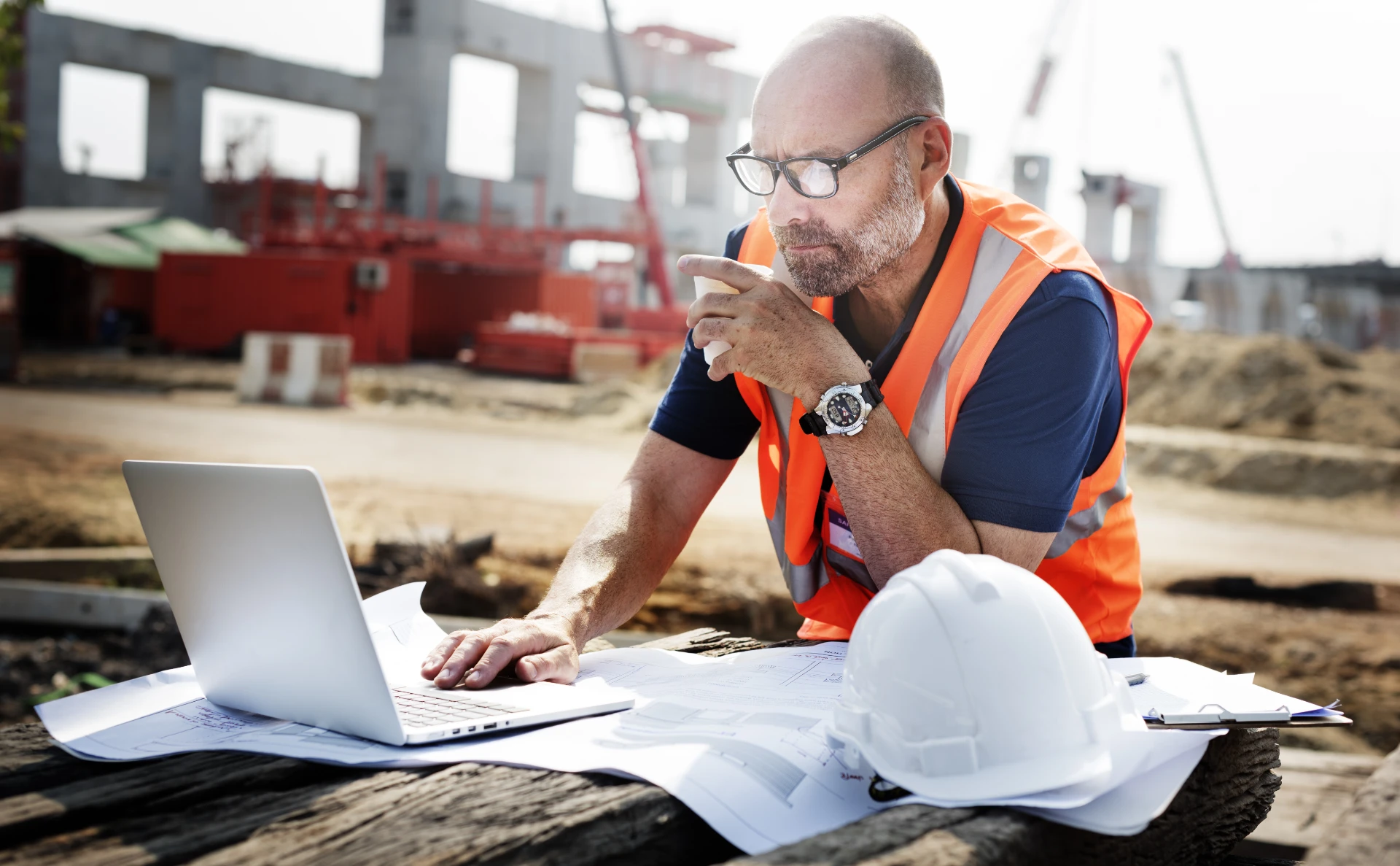 Bauleiter überprüft einen Bauzeitenplan auf einem Laptop auf einer aktiven Baustelle