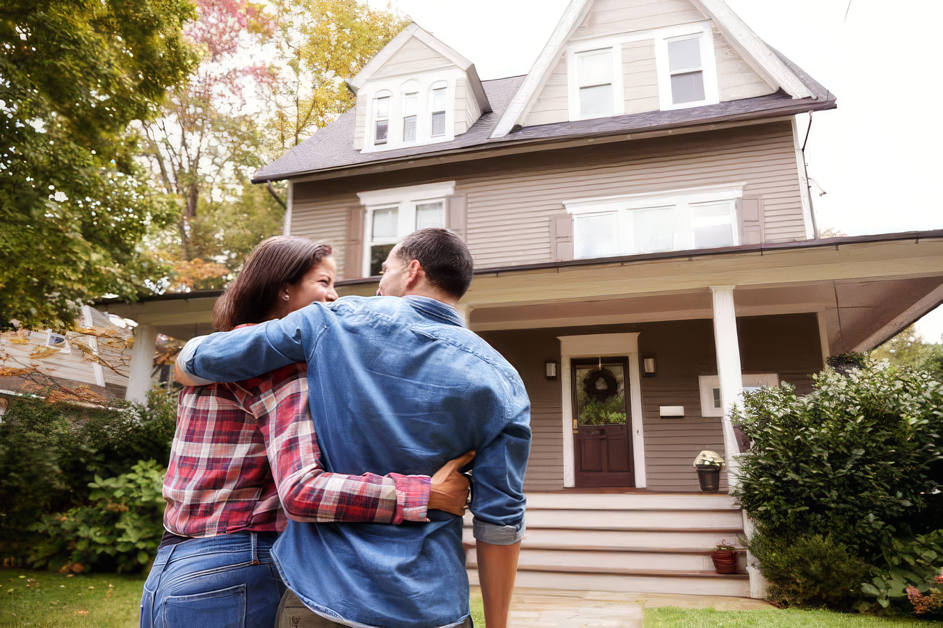 Couple hugging and smiling while looking at a large two-story house with a front porch.