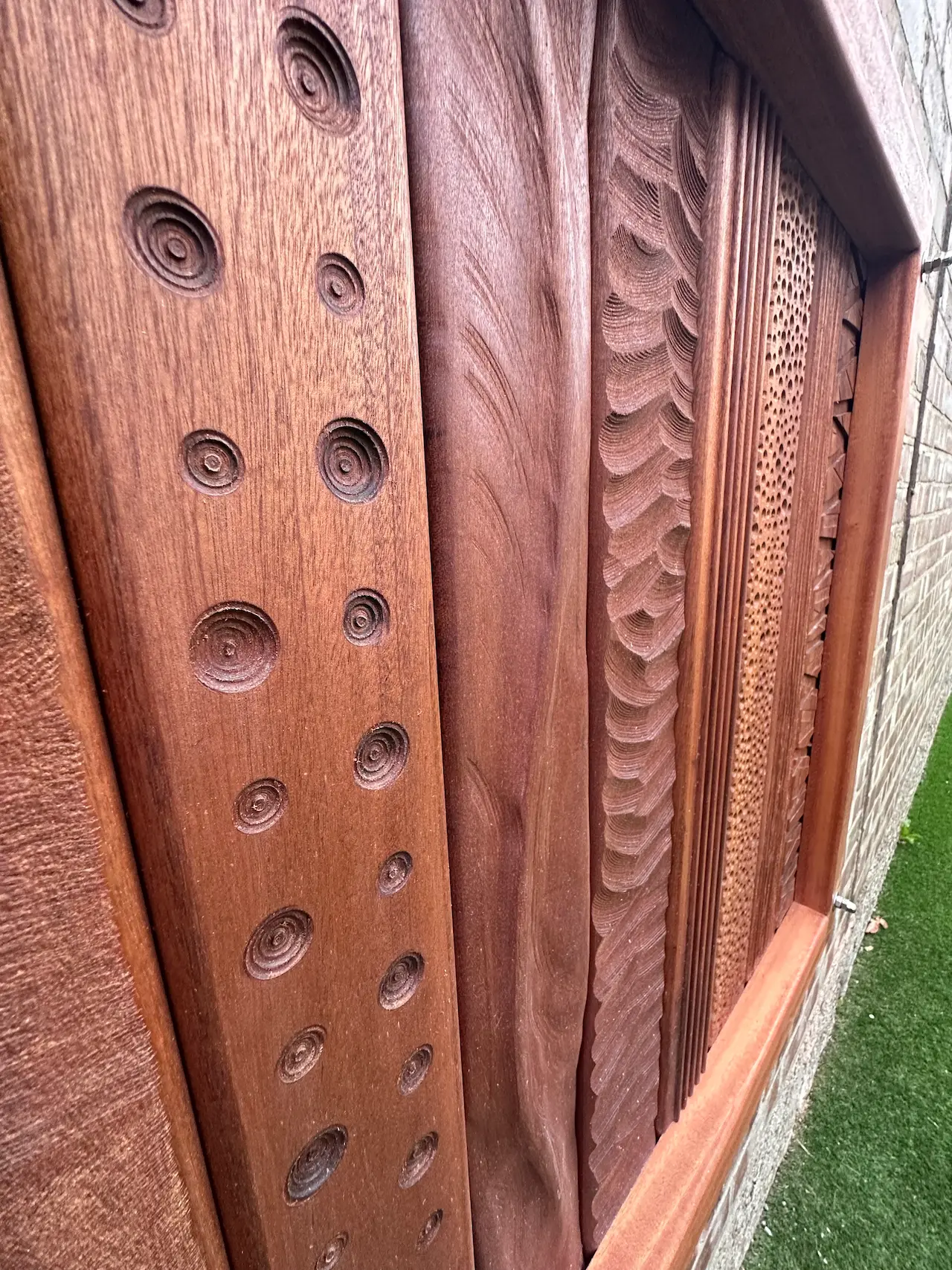 Close-up of a wooden tactile panel with multiple carved patterns including concentric circles, smooth curves, scalloped edges, and small indentations.