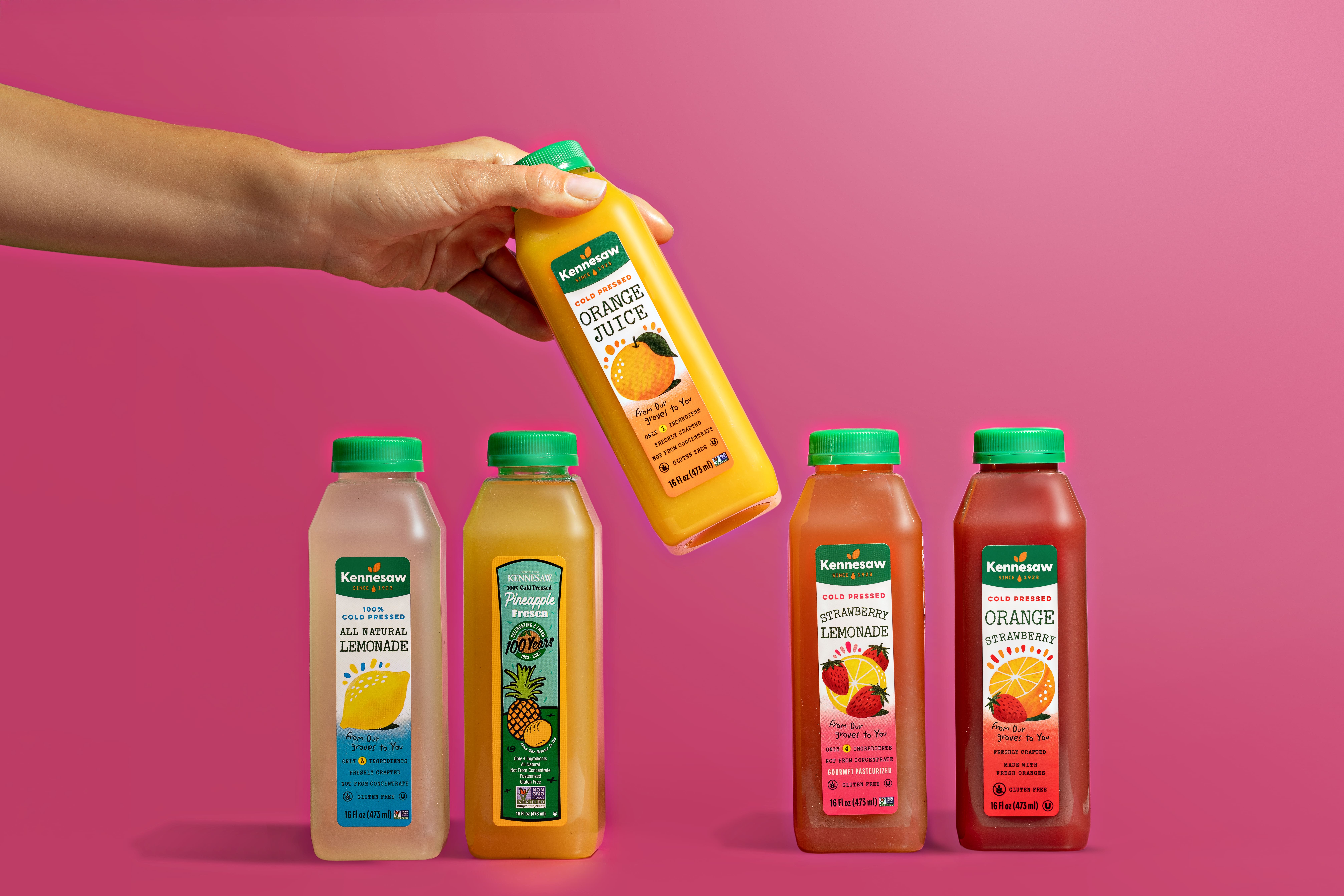 Manicured Hand Pouring Kennesaw Orange Juice into a Glass on a Table Next to Sliced Oranges