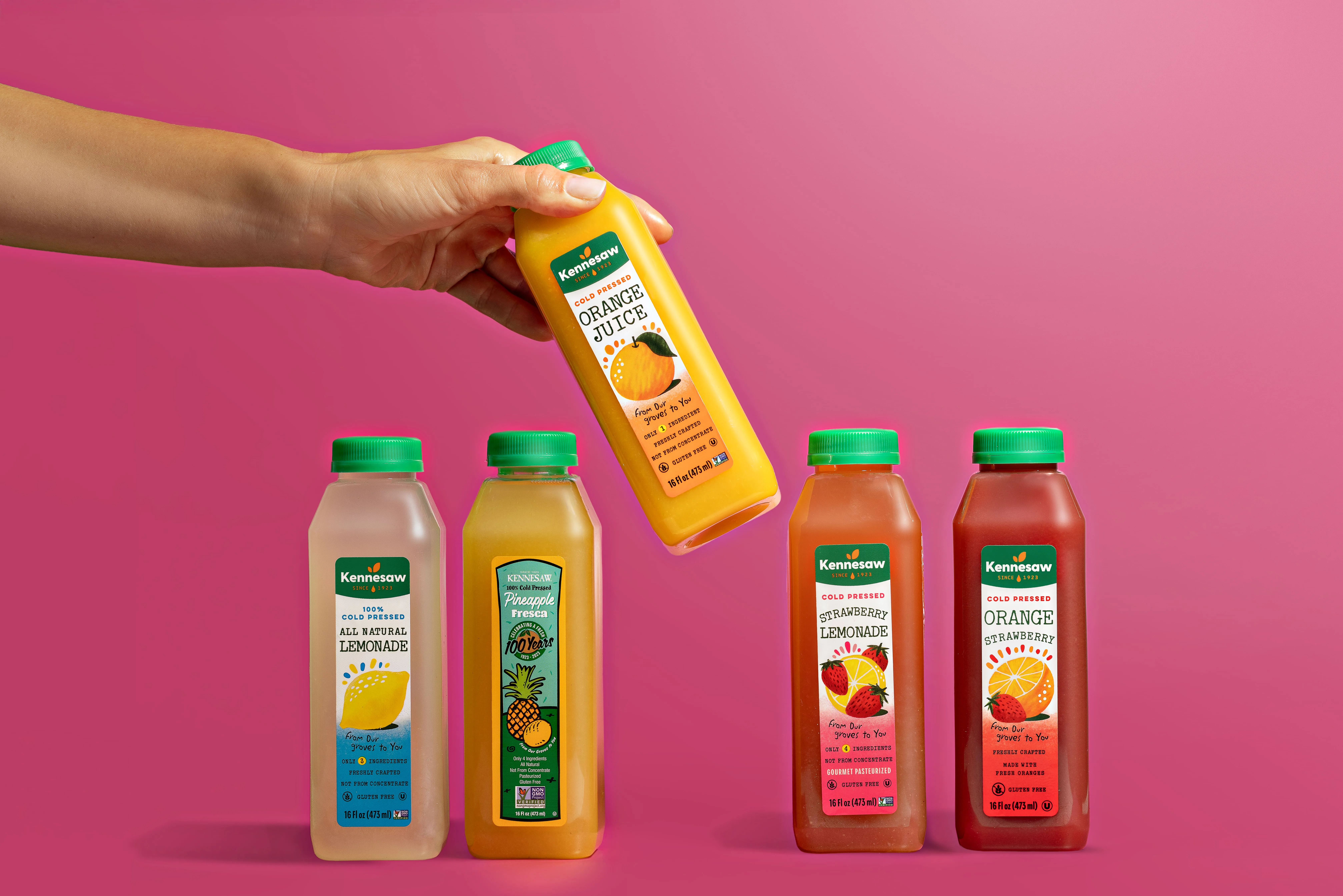 Manicured Hand Pouring Kennesaw Orange Juice into a Glass on a Table Next to Sliced Oranges