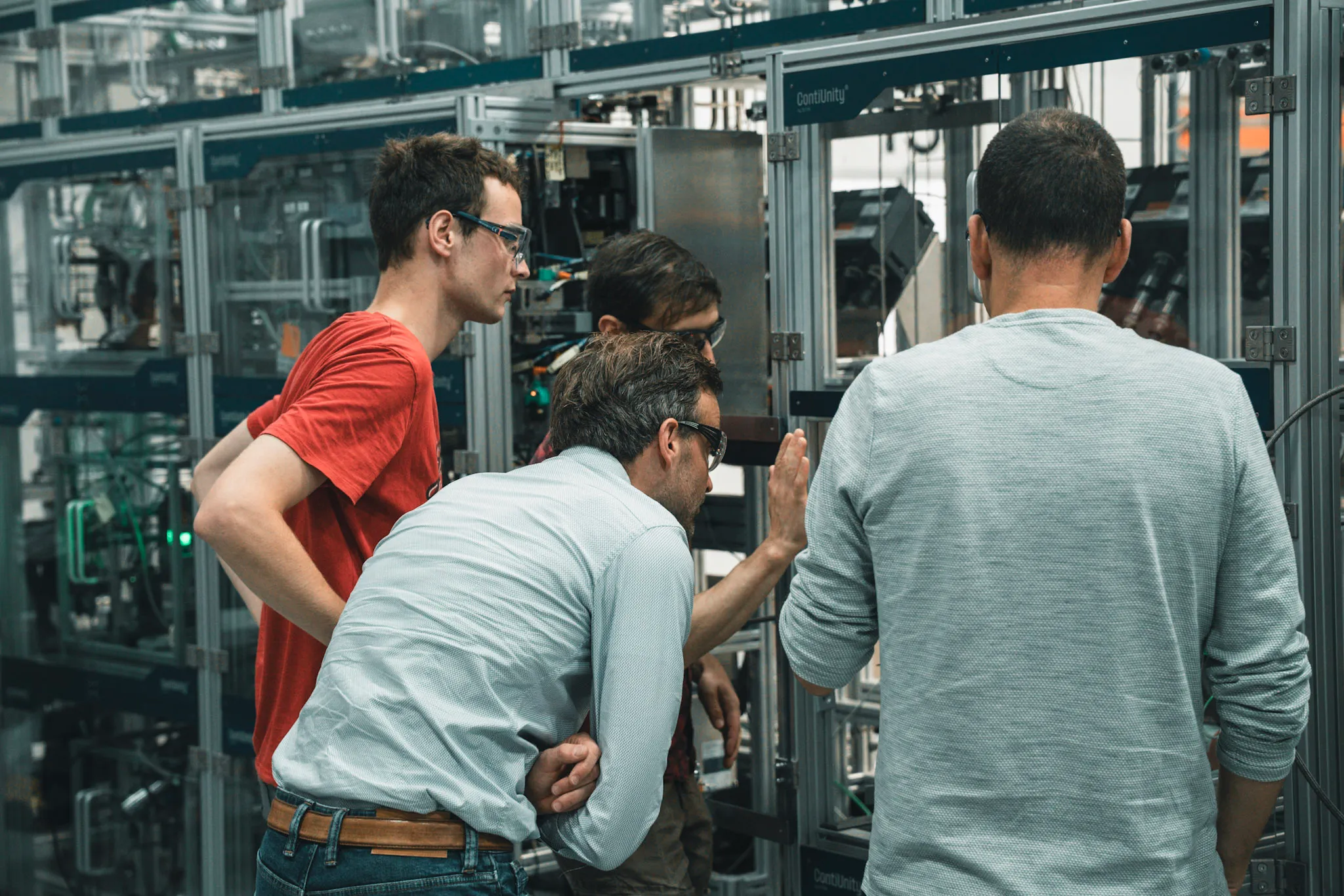 Four men wearing protective glasses inspecting high-tech machinery labeled ContiUnity in an industrial setting.