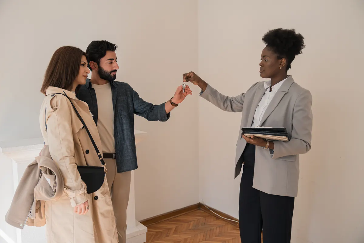 A female real estate agent handing a couple the keys to their new home purchase.