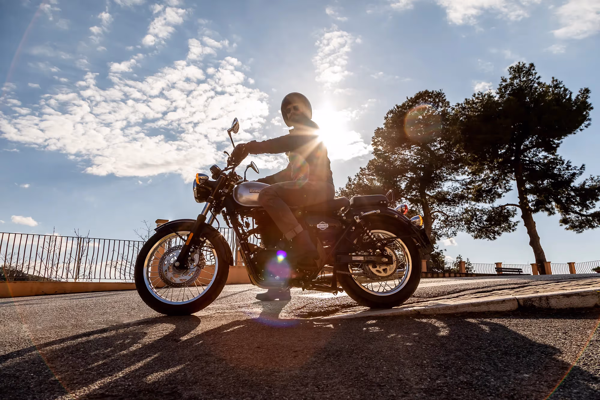 A rider on a Benelli IMPERIALE 400 is resting in the backlight of the sunlight.
