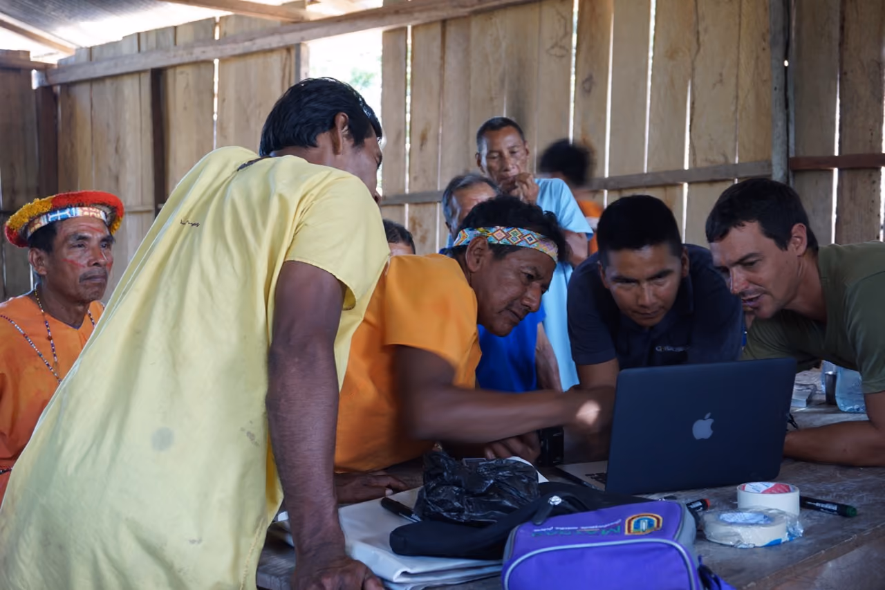 Indigenous community members and Awana Digital staff collaborating around a laptop in a wooden field structure