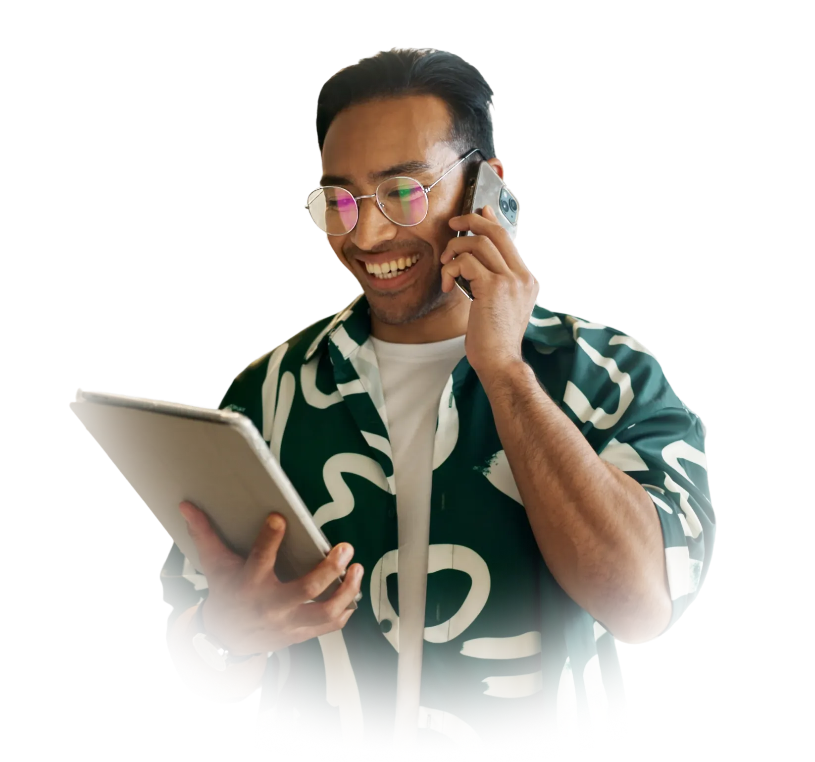 Smiling man wearing glasses and patterned shirt talking on smartphone while holding a tablet.