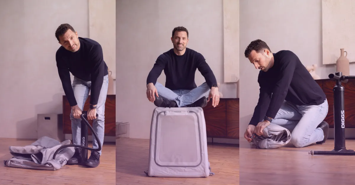 Smiling man in a dark blue shirt with rolled-up sleeves and woman with blonde hair wearing a black blazer and blue pants sitting on a beige sofa with woven baskets on the table in front.
