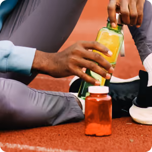 Person squeezing yellow mustard bottle into a red jar on a red running track surface.