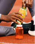 Person squeezing yellow mustard bottle into a red jar on a red running track surface.