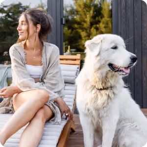 Smiling woman sitting on wooden steps next to a large white fluffy dog outdoors.