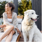 Smiling woman sitting on wooden steps next to a large white fluffy dog outdoors.