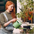 Young woman with red hair watering plants with a green watering can outdoors.