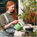 Young woman with red hair watering plants with a green watering can outdoors.