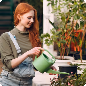 Young woman with red hair watering plants with a green watering can outdoors.