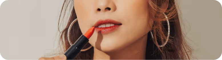 Close-up of a woman applying red lipstick with large hoop earrings visible.