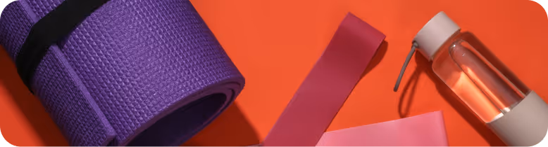 Rolled purple yoga mat, pink resistance bands, and a clear water bottle on an orange surface.