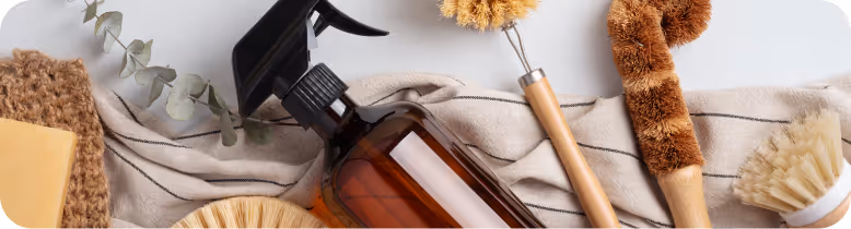 Cleaning brushes and a spray bottle arranged on a cloth surface, including a wooden brush with a long handle and natural bristles.