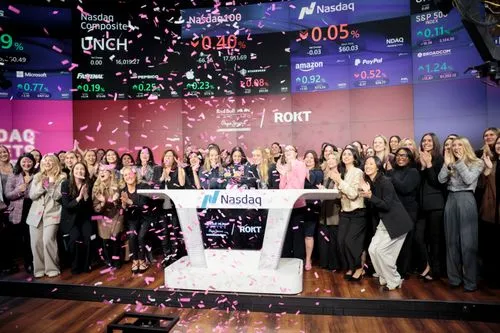 Group of diverse women clapping and celebrating at Nasdaq podium with pink confetti falling.