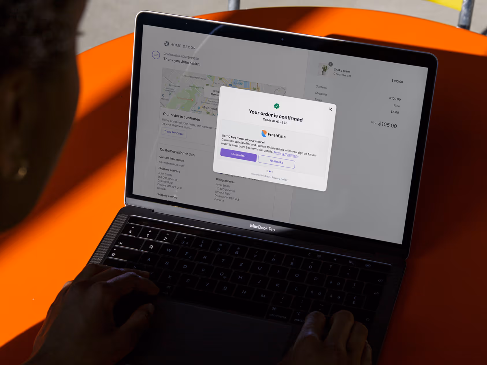 Person using MacBook Pro showing an online order confirmation screen with delivery details and an offer popup.