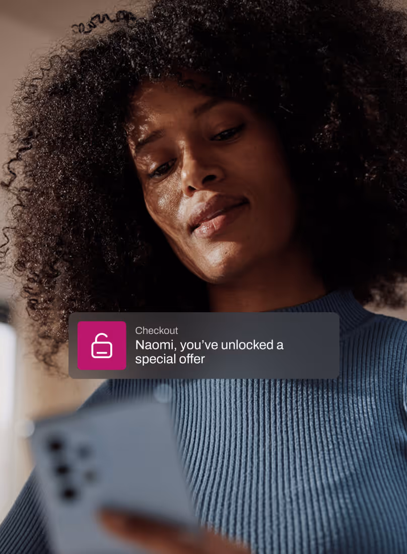 A woman in a blue ribbed sweater looks down at her smartphone with a soft smile. A checkout message overlay reads: “Naomi, you’ve unlocked a special offer,” suggesting real-time incentives during online shopping.