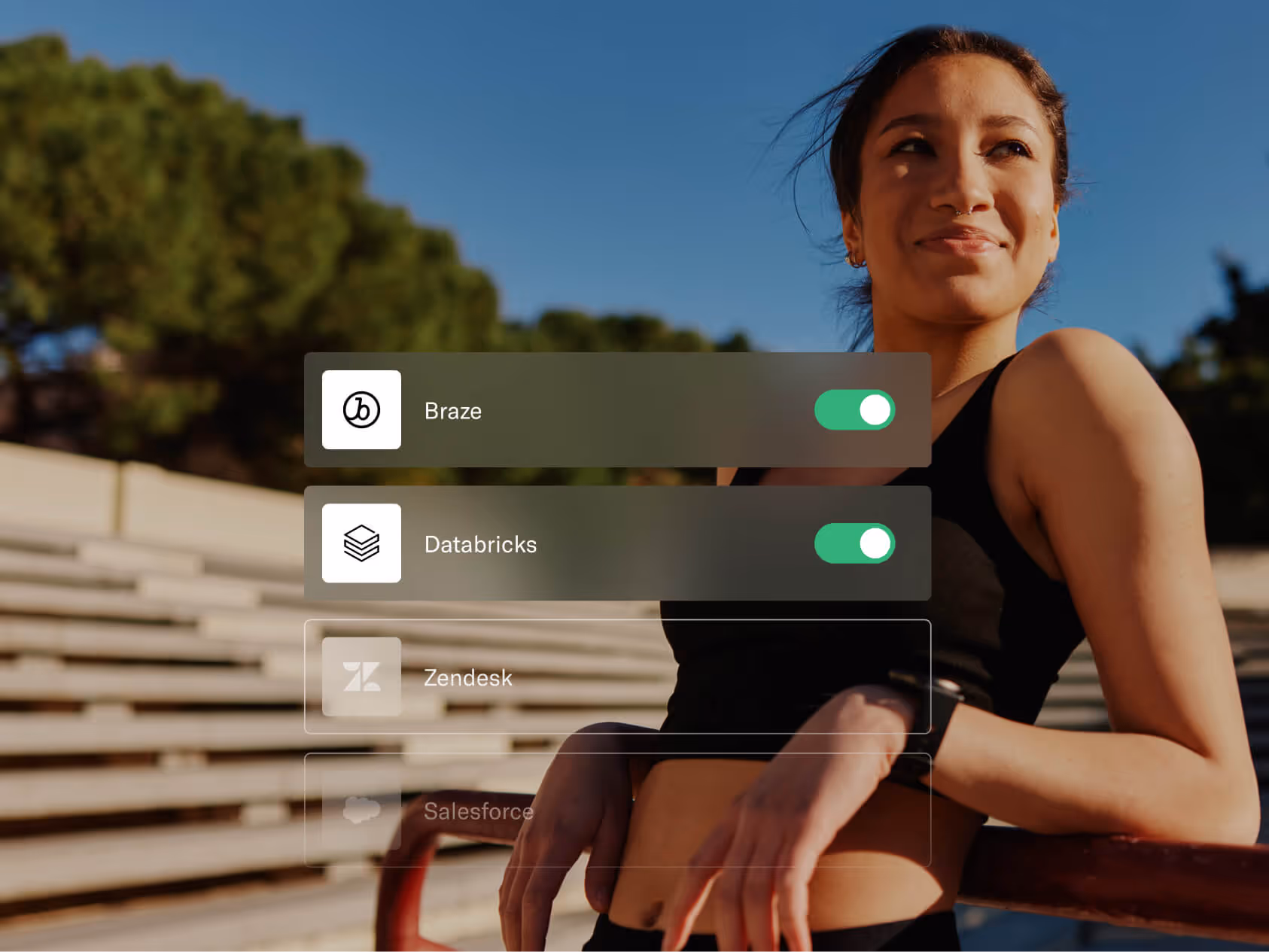 Una mujer con ropa deportiva se apoya casualmente en una barandilla roja en un estadio al aire libre y sonríe con confianza a la luz del sol. Los botones superpuestos muestran que «Braze» y «Databricks» están activados, mientras que «Zendesk» y «Salesforce» están atenuados. La configuración y la tecnología superpuestas transmiten un mensaje de empoderamiento e integraciones simplificadas.