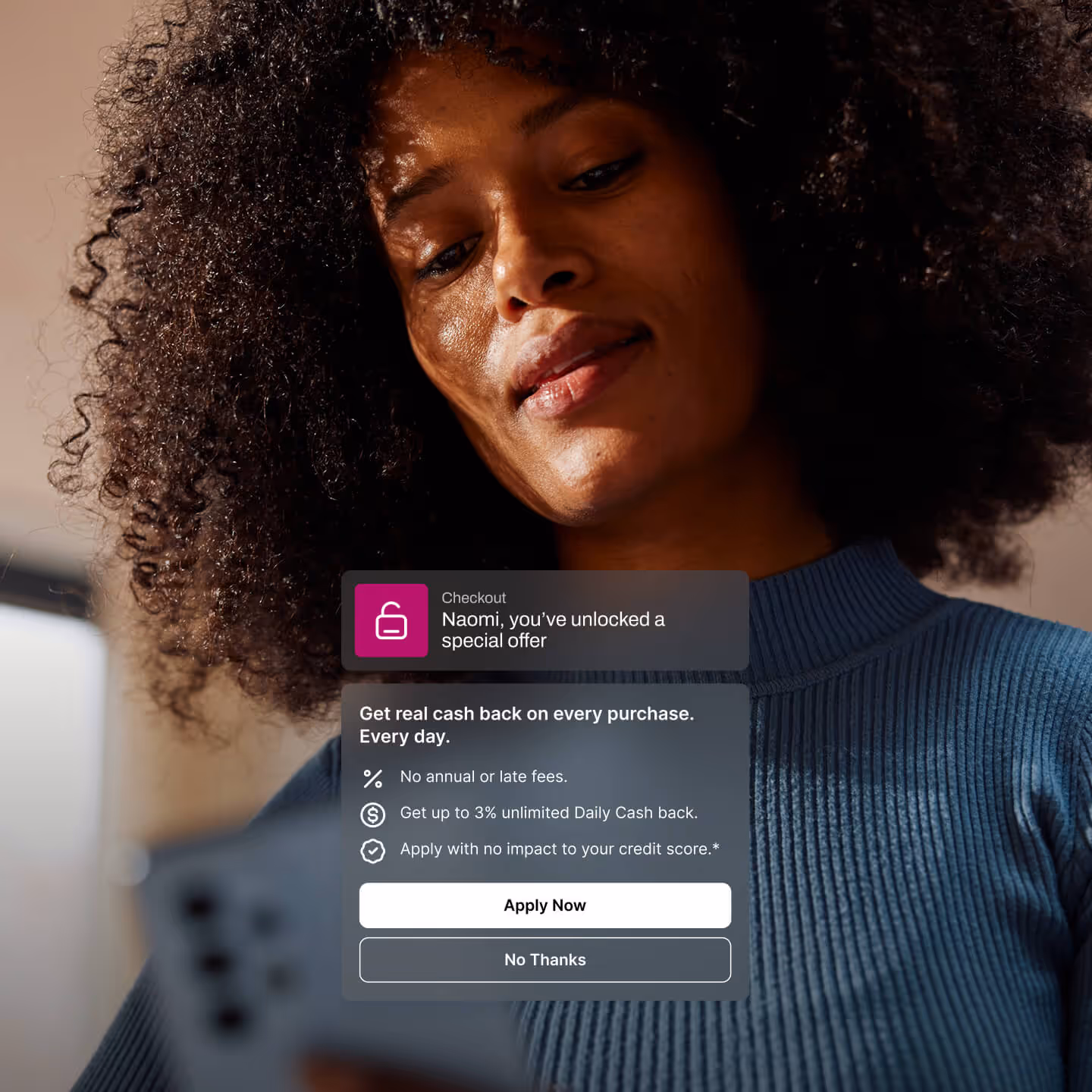 Close-up of a woman with curly hair and a blue sweater looking at her smartphone with a digital offer overlay about unlocking a special cash back deal.