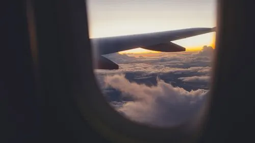 View of an airplane wing above clouds during sunset from a passenger window.