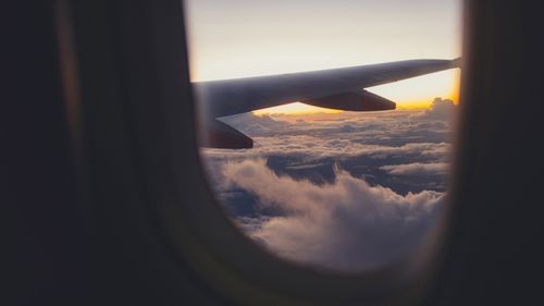 View of an airplane wing above clouds during sunset from a passenger window.