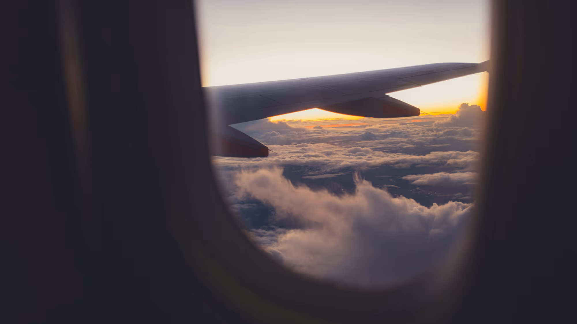 View of an airplane wing above clouds during sunset from a passenger window.