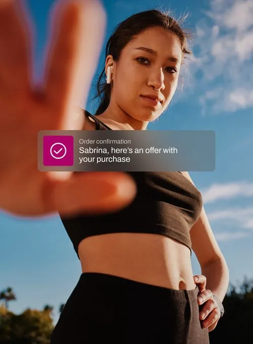 Young woman in black sportswear reaching hand toward the camera outdoors under blue sky with a notification overlay about order confirmation and purchase offer.