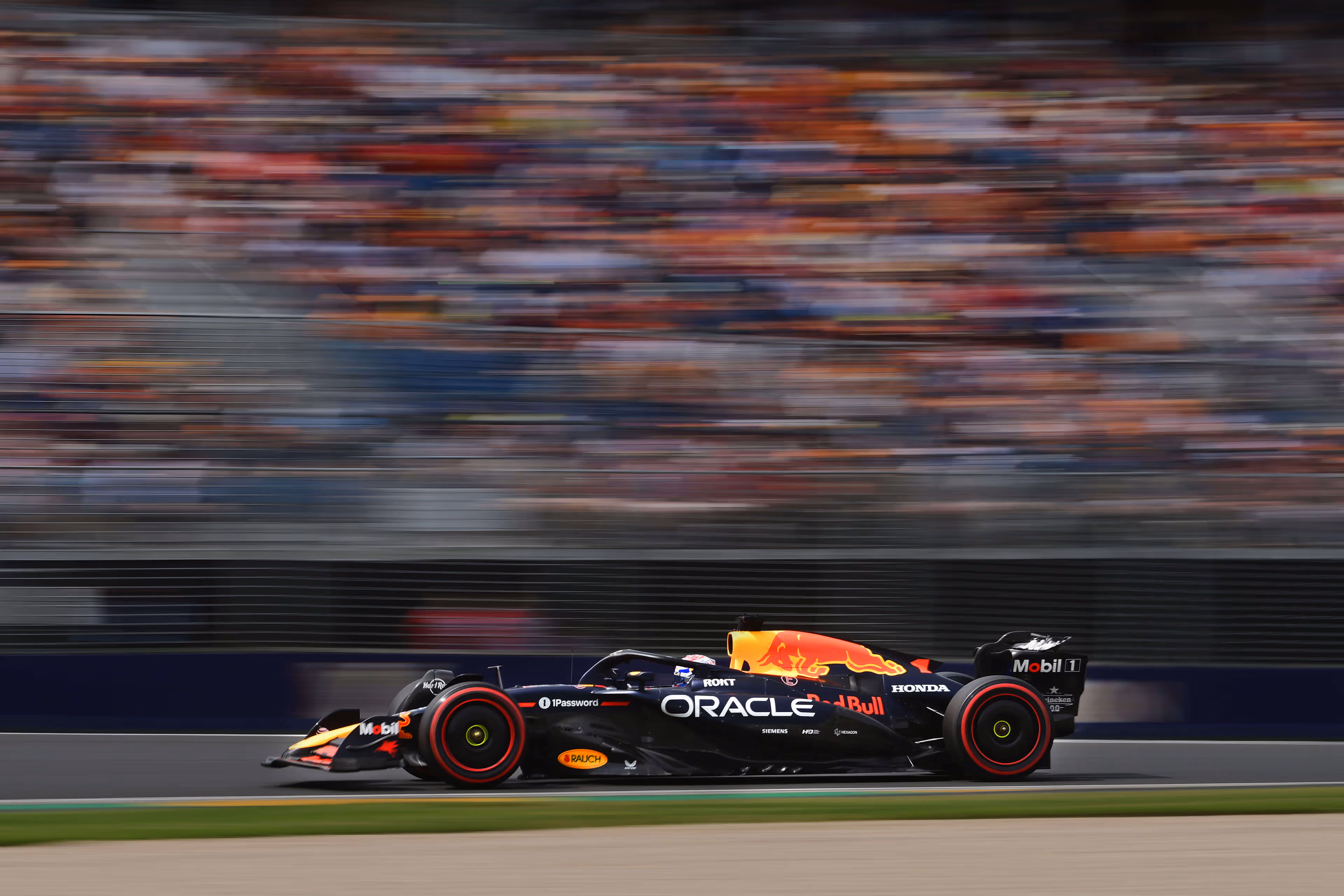 Red Bull Racing Formula 1 car speeding on a race track with blurred crowd stands in the background.