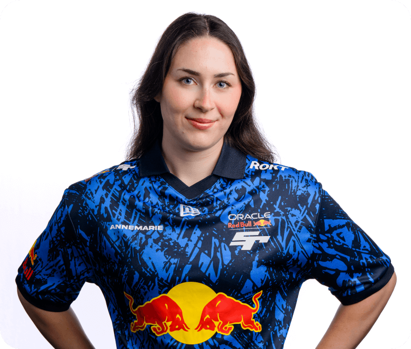 A woman with long dark hair poses confidently in a studio portrait wearing a blue and black Oracle Red Bull Racing esports jersey with the name “ANNEMARIE” on the chest. She smiles subtly with her hands on her hips.