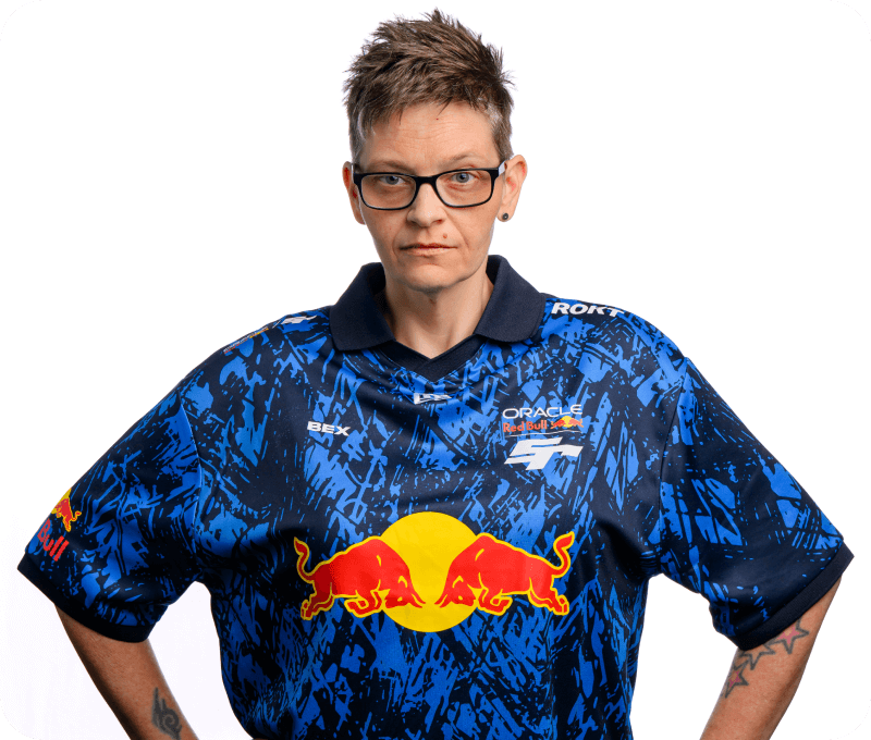 A person with short spiked hair and glasses stands with a serious expression, hands on hips, wearing a bold Oracle Red Bull Racing esports jersey labeled “BEX.” The background is clean and white, emphasizing the subject.