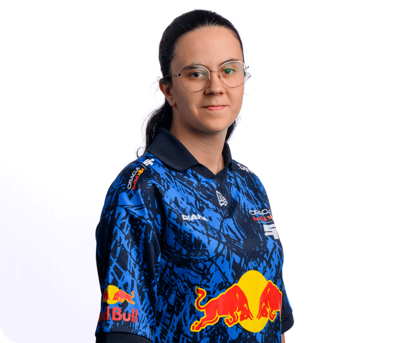 A woman with glasses and a ponytail gives a calm, neutral smile while standing in a Red Bull Racing esports jersey with the name “DIANA.” Her posture is relaxed, angled slightly sideways in front of a plain white backdrop.