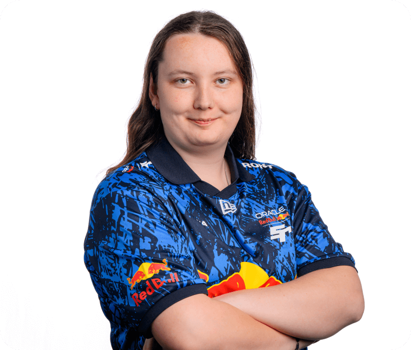 A woman with straight, shoulder-length hair crosses her arms with a slight smile, wearing a Red Bull Racing esports jersey with the name partially obscured. She appears confident and composed against a white background.