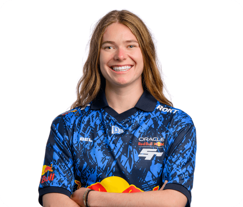 A smiling young person with long, light brown hair stands with arms crossed, wearing a blue Oracle Red Bull Racing esports jersey with abstract patterns and sponsor logos. The background is plain white.