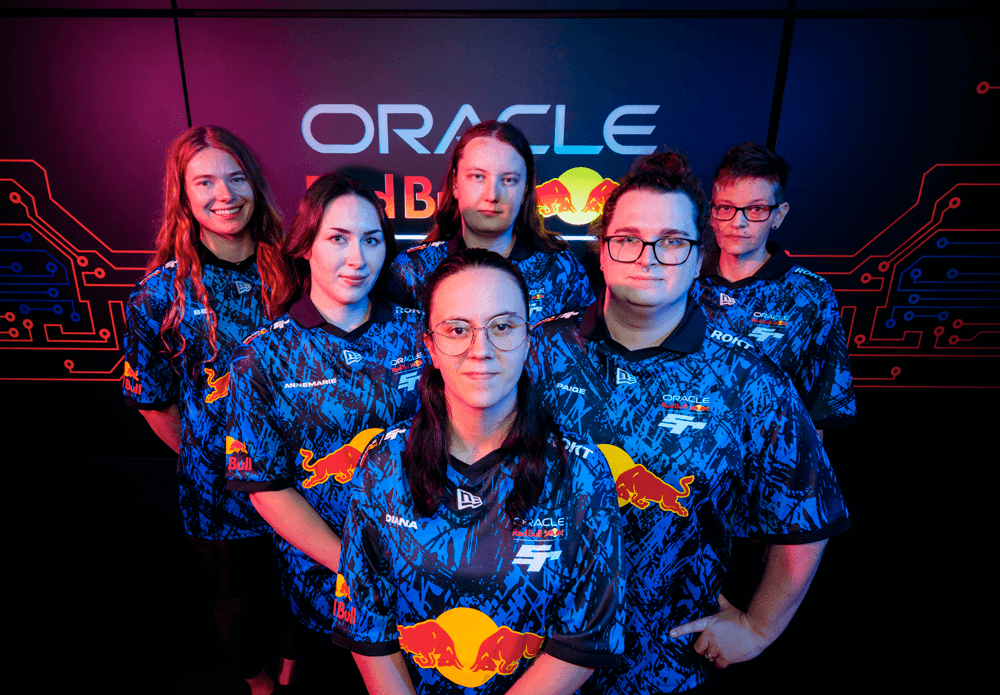 Six esports team members wearing matching Oracle Red Bull Racing jerseys pose together under dramatic blue and pink lighting. The group, a mix of men and women, stands confidently in front of a tech-inspired backdrop with circuit board graphics and the "Oracle Red Bull Racing" logo prominently displayed. Each jersey features sponsor logos including Red Bull and New Era, with some team members’ names like “Diana” and “Jannemarie” visible on the front. The mood is focused and proud, emphasizing teamwork, inclusion, and professional gaming.