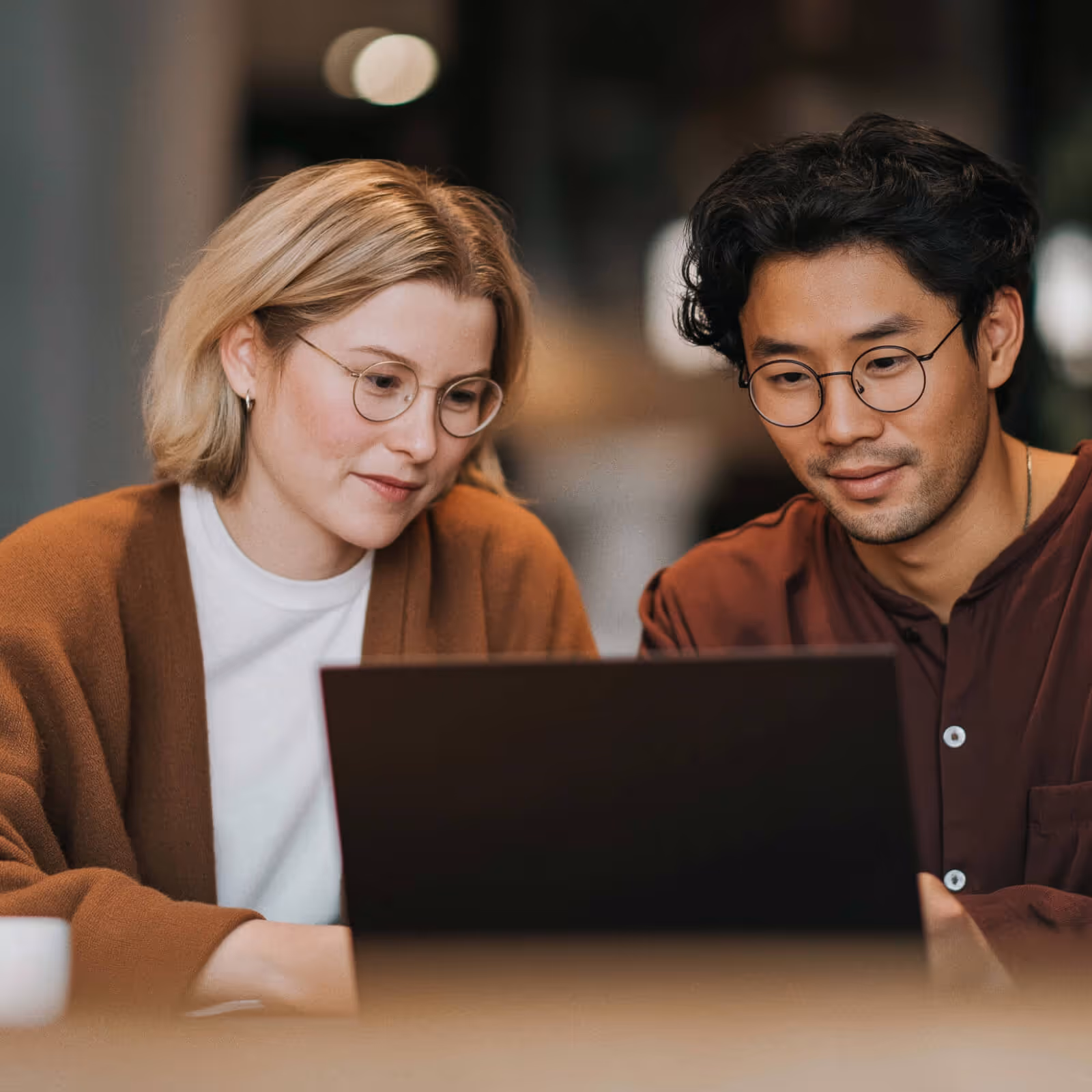 A young woman and man wearing glasses looking at a laptop screen together.