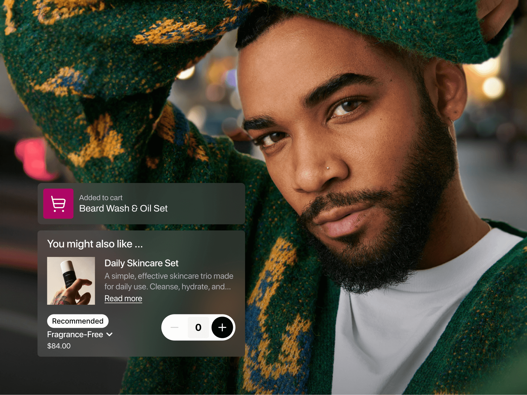 A man with a neatly groomed beard and nose piercing, wearing a green sweater with yellow patterns, poses confidently in an urban night setting. Overlaid is a shopping notification showing he added a “Beard Wash & Oil Set” to his cart. A recommendation for a $84 Daily Skincare Set appears below, with a quantity selector and a dropdown for fragrance options.