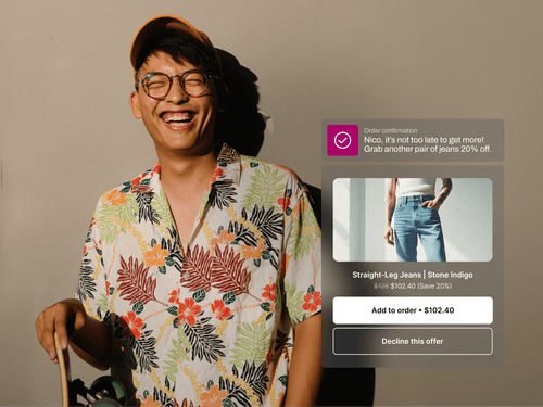 A smiling man in a floral shirt and orange cap leans against a wall holding a skateboard, bathed in warm sunlight. A notification says, “Nico, it’s not too late to get more!” offering him a 20% discount on a second pair of jeans. A product card below displays “Straight-Leg Jeans | Stone Indigo” with the discounted price and buttons to add the item or decline.