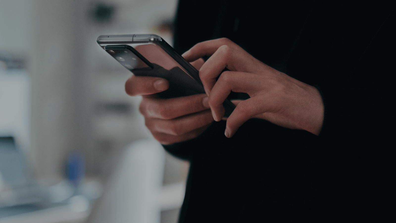 Close-up of a person’s hands holding and typing on a smartphone, with the screen angled slightly upward. The blurred indoor background and focused gesture suggest texting, mobile browsing, or managing tasks on a digital device.