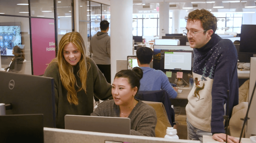 Three colleagues collaborating and looking at a computer screen in a modern open office space.