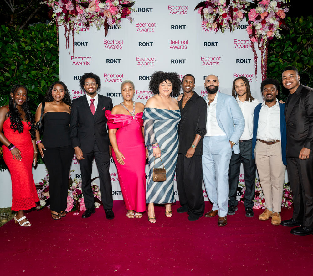 Group of ten well-dressed people posing on a red carpet in front of a Beetroot Awards and ROKT branded backdrop with floral decorations above.