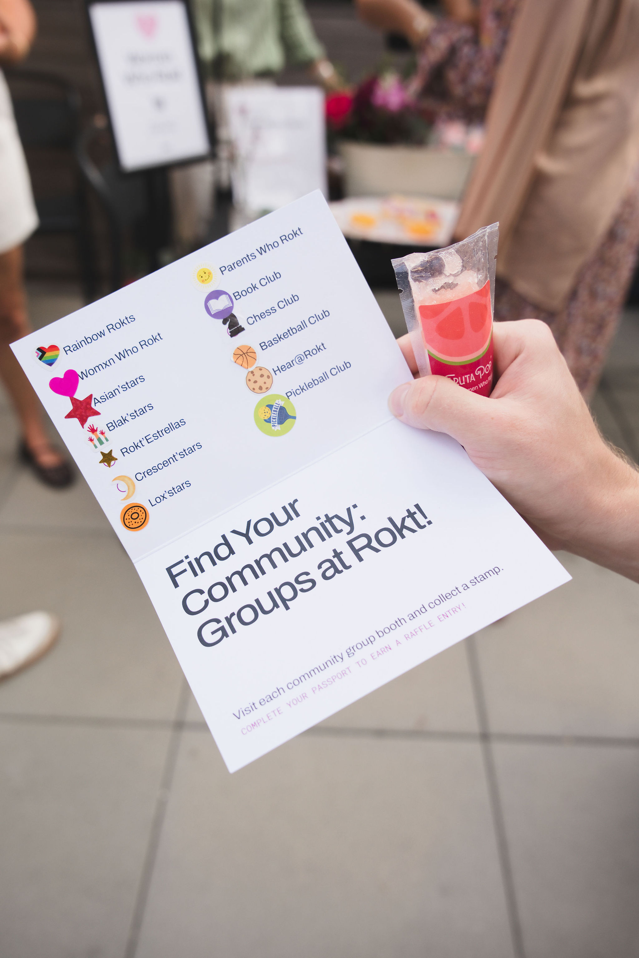 Hand holding a flyer listing community groups at Rokt with icons and a red popsicle.